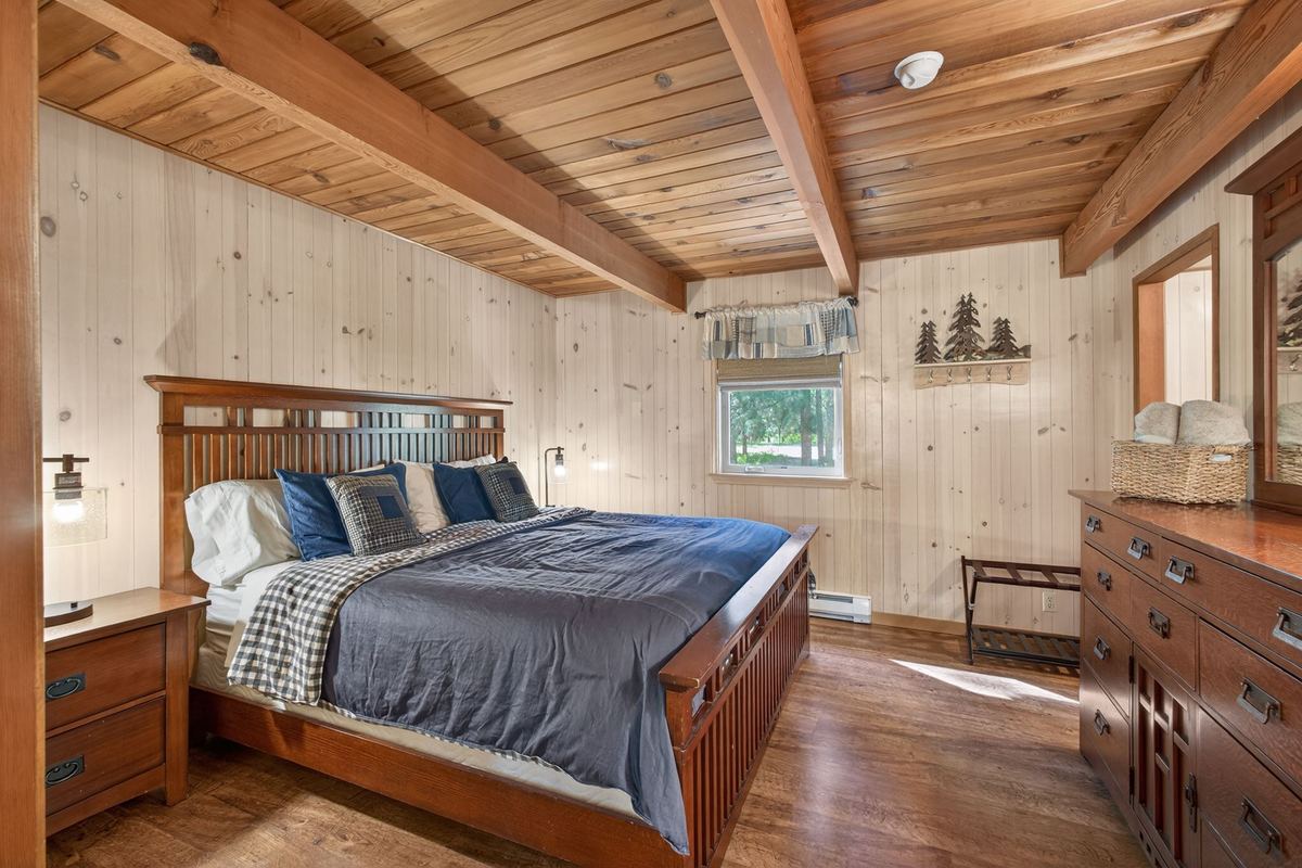 King bedroom with pine-paneled walls and a beamed ceiling